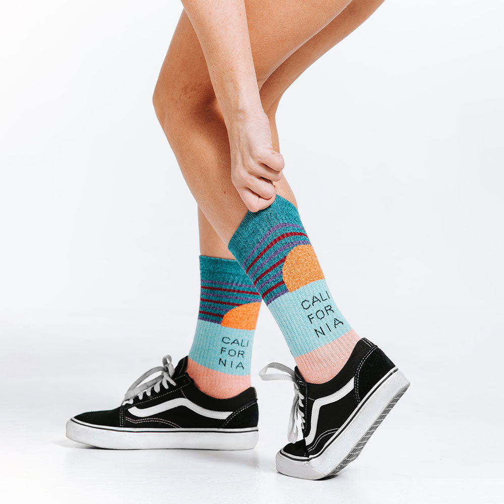Person wearing colorful lifestyle compression socks with text and black sneakers on a white background