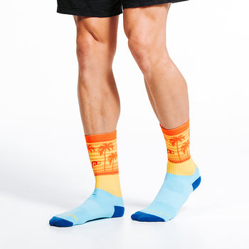Man wearing Crew length compression sock blue and orange with sunset and palm trees