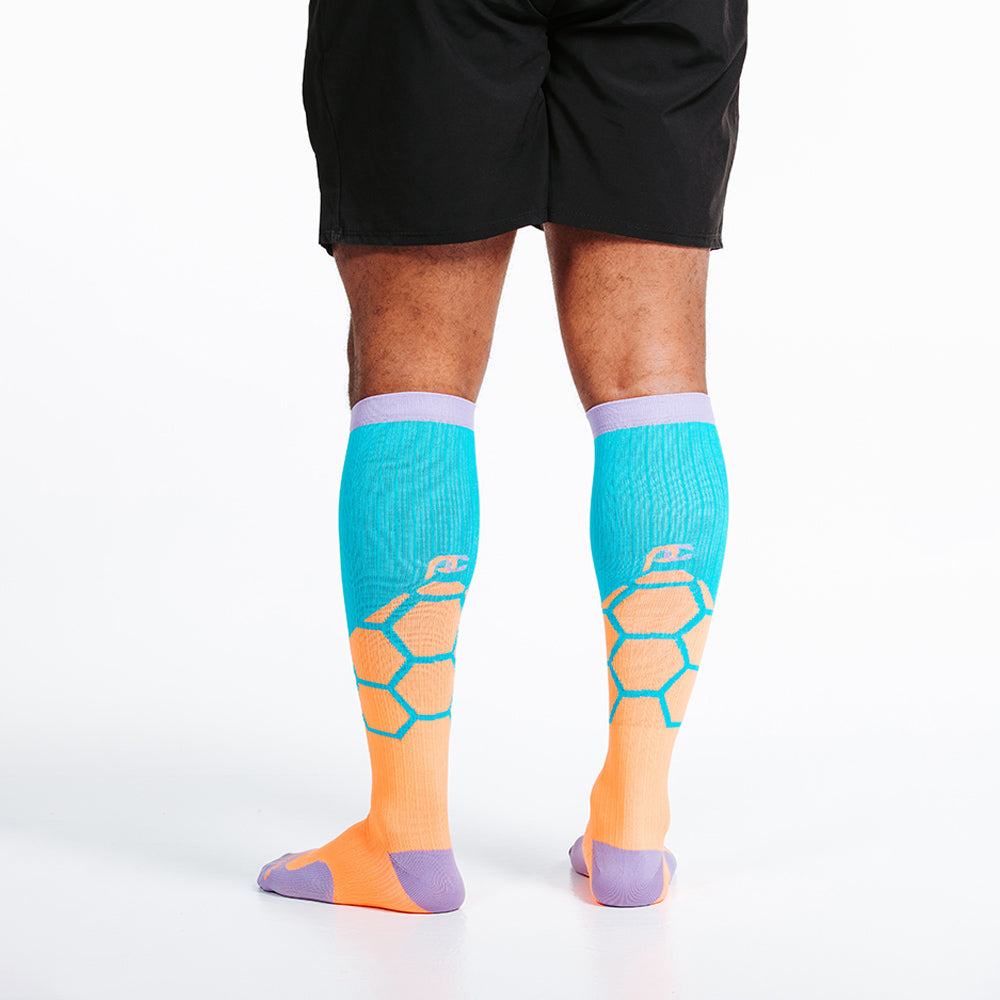 Orange BOOM design in PRO Compression knee high compression socks. Bright orange and teal design with lavender cuff, toe and heel boxes. On model, close up rear view