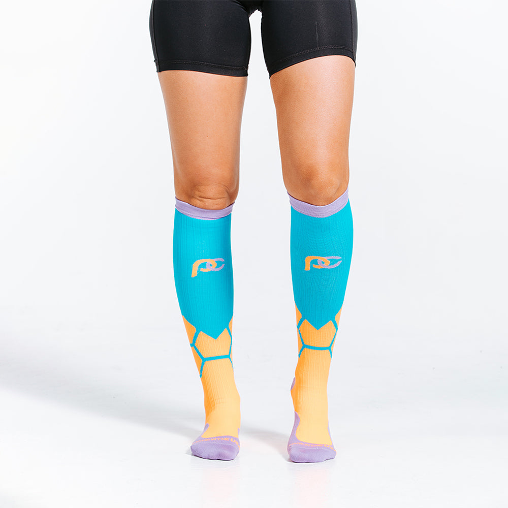 Orange BOOM design in PRO Compression knee high compression socks. Bright orange and teal design with lavender cuff, toe and heel boxes. Close up on feet of female model