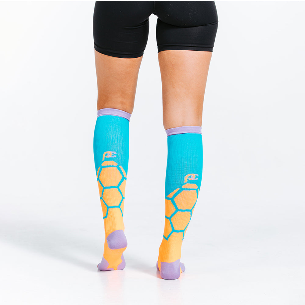 Orange BOOM design in PRO Compression knee high compression socks. Bright orange and teal design with lavender cuff, toe and heel boxes. Rear-view on model