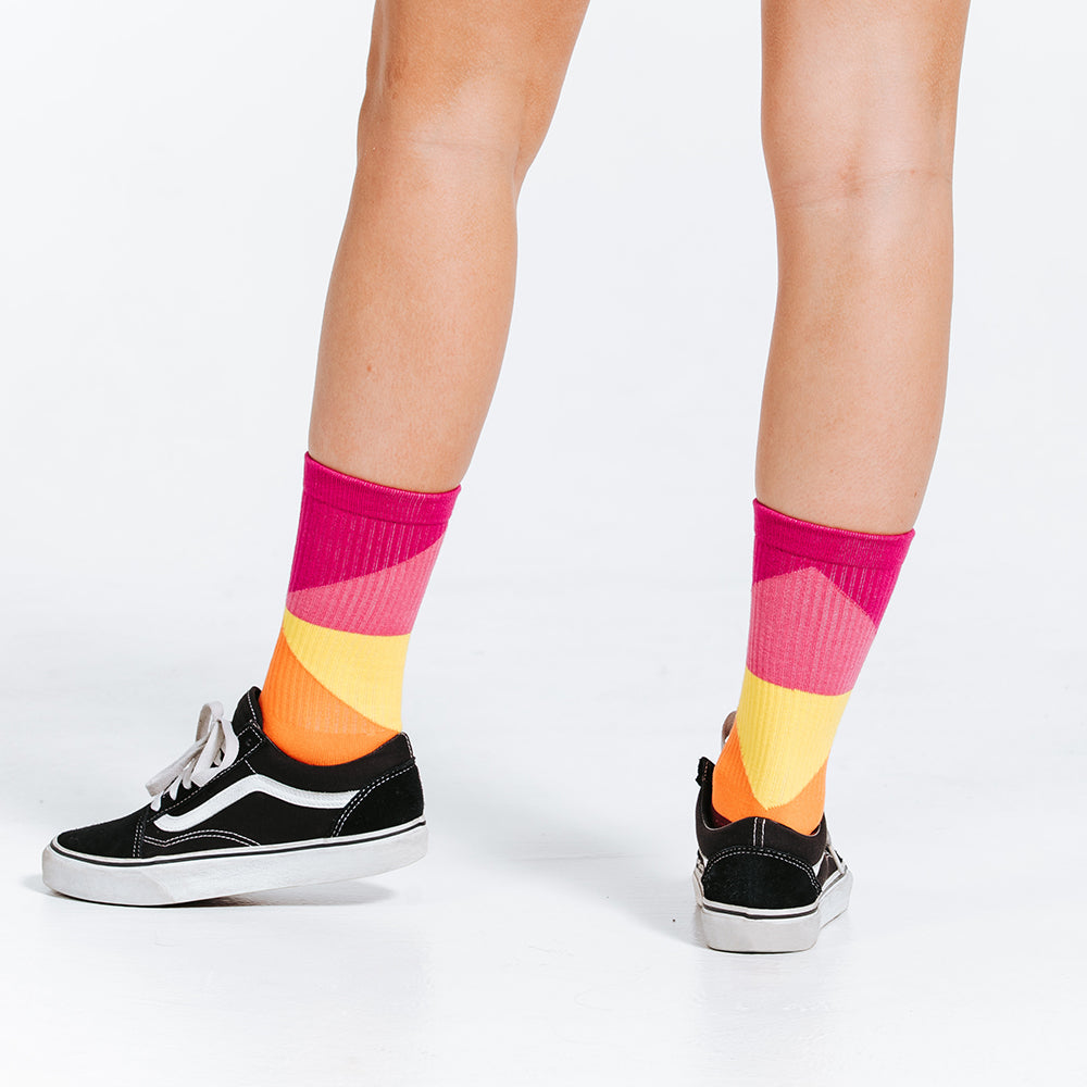 Colorful compression socks, crew length, with pink, yellow, orange, and red - close up of feet, rear view